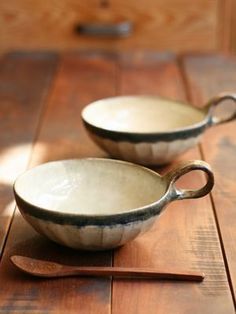 two white bowls sitting on top of a wooden table with spoons in front of them