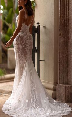 a woman in a white wedding dress standing by a wall with her back to the camera