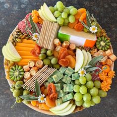 a platter filled with cheese, crackers, grapes, apples and other fruits