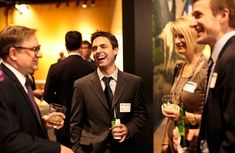 a group of people standing next to each other holding wine glasses and smiling at the camera