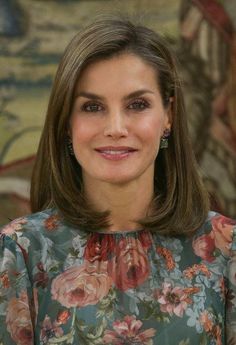 a woman in a floral dress smiles at the camera while wearing large earrings on her left ear