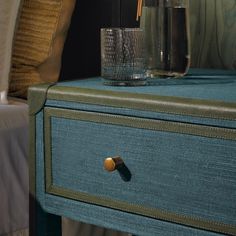 a close up of a drawer with a glass on it and a bed in the background