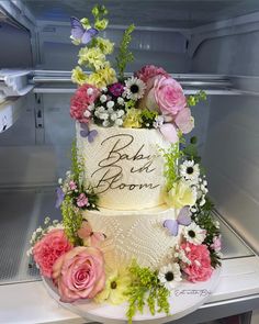 a three tiered cake with flowers and butterflies on the top is sitting in an open refrigerator