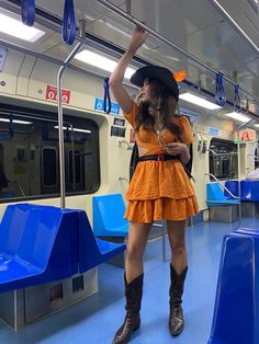 a woman in an orange dress and cowboy hat standing on a subway train with blue seats