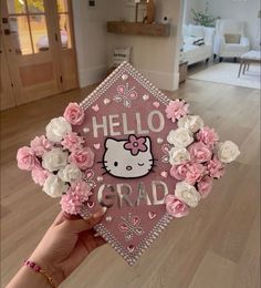 someone is holding up a graduation cap decorated with pink and white flowers in front of a living room