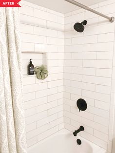 a white tiled bathroom with black fixtures and shower head in the bathtub next to curtain