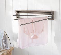 an ironing board and clothes hanging on a wall next to a drying rack with two towels