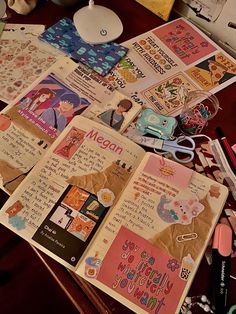 an open book sitting on top of a wooden table next to pens and pencils