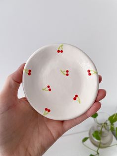 a hand holding a small white bowl with red berries on the rim and green leaves