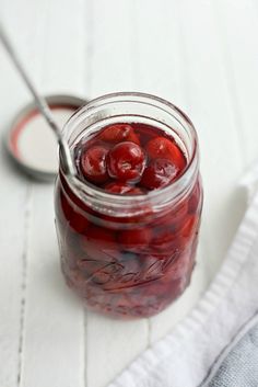 a jar filled with cherries sitting on top of a white table next to a spoon