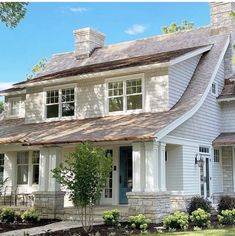 a white house with blue door and windows on the front porch is surrounded by greenery