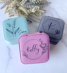 three different colored cases sitting on top of a white table next to some flowers and branches