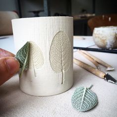 a cup with leaves on it sitting next to some crochet needles and yarn