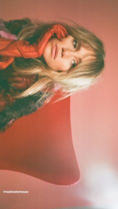 a woman with long blonde hair standing in front of a pink wall