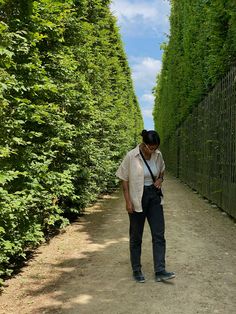 a man walking down a dirt road next to tall green trees on either side of him