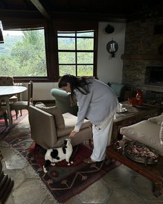 a woman bending over to pet a black and white dog on a rug in a living room