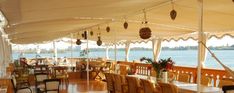 an outdoor dining area with tables and chairs on the deck next to the water is covered in white drapes