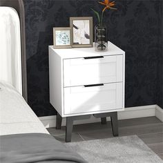 a white nightstand with two pictures on top of it next to a bed and wall