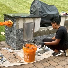 a woman is painting the outside of a bbq with an orange bucket on it