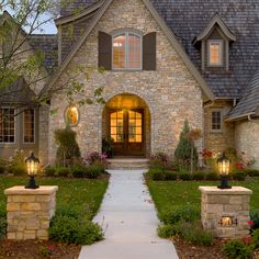 a stone house with lights on the front door and walkway leading up to it's entrance