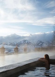 a woman sitting in a hot tub with mountains in the background