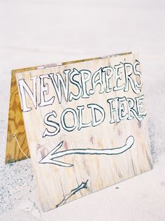 a wooden sign that says news papers sold here on the ground next to an arrow