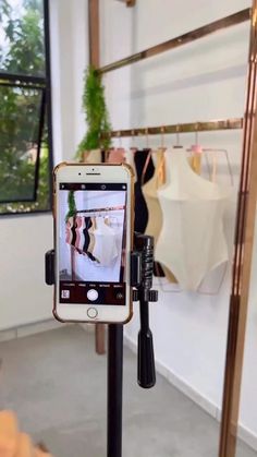 a cell phone that is sitting on a tripod in front of a rack with clothes