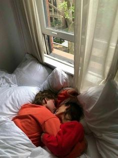 two children are sleeping in their bed by the window, one is wearing an orange shirt