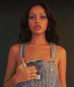 a woman in overalls holding a cell phone and pointing at the camera with her finger