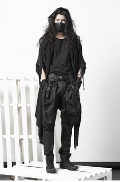 a man with long hair wearing black clothes and a mask standing in front of a white wall