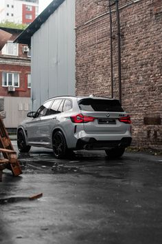 a silver car parked in front of a brick building next to a wooden ladder on the street