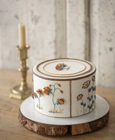 a decorated cake sitting on top of a wooden table next to a candle and some flowers