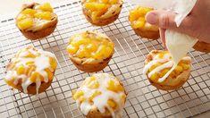 a person is spreading icing on some muffins that are sitting on a cooling rack