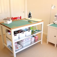 a sewing table with lots of crafting supplies on the top and bottom shelves in front of it