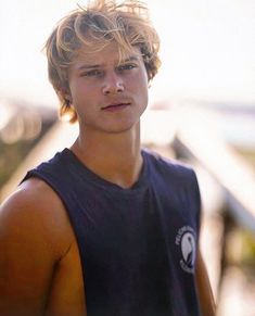 a young man in a tank top is posing for the camera with his hand on his hip