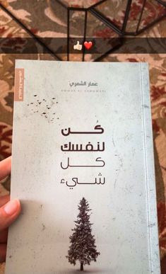 a person holding up a book with arabic writing and a tree on the front cover