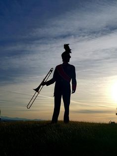 a man holding a trombone in his hand while standing on top of a grass covered field