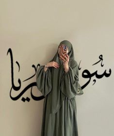 a woman in a green dress is holding up a paper flower with arabic writing on the wall behind her