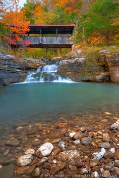 a small waterfall in the middle of a forest next to a wooden bridge over rocks