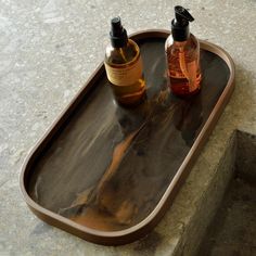 two bottles of alcohol are sitting on a tray that sits on the concrete floor next to stairs