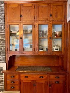 an old wooden china cabinet with glass doors on the top and bottom, in front of a brick wall