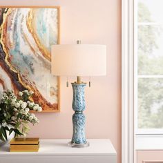 a blue vase with flowers on a white table next to a lamp and window in a pink room