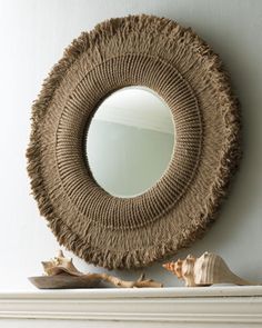 a round mirror hanging on the wall above a mantle with seashells and sea shells