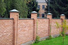 a brick fence with green grass and trees in the background