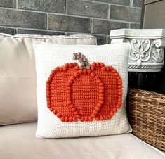 a crocheted pumpkin pillow sitting on top of a couch next to a wicker basket