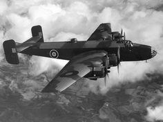 an old airplane flying in the sky above some clouds and land below it is black and white