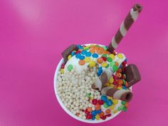 a cup filled with candy and marshmallows on top of a pink surface