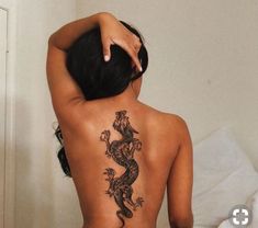 a woman with a tattoo on her back is standing in front of a white wall