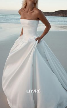 a woman in a white wedding dress standing on the beach with her hands on her hips