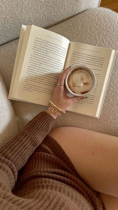 a woman reading a book while holding a cup of coffee